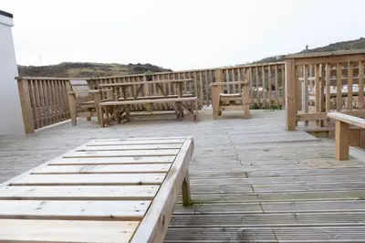 a wooden deck with benches and tables on it at Pollymoor Beach House in Holywell Bay