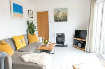 a living room with a gray couch and a wood stove at Pollymoor Beach House in Holywell Bay