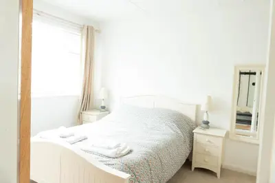 a white bedroom with a bed and a mirror at Hoblyns Cove in Holywell Bay