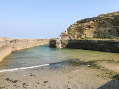a body of water next to a stone wall at Lighthouse Lofts - Godrevy in Camborne