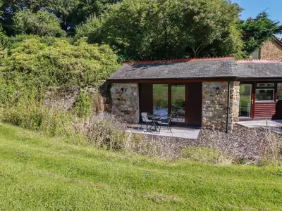 a stone cottage with a table and a chair in a field at Peony Cottage in St Austell