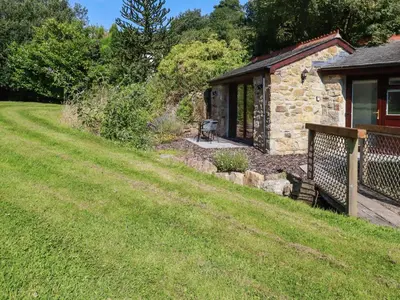 a stone cottage with a bench next to a yard at Peony Cottage in St Austell