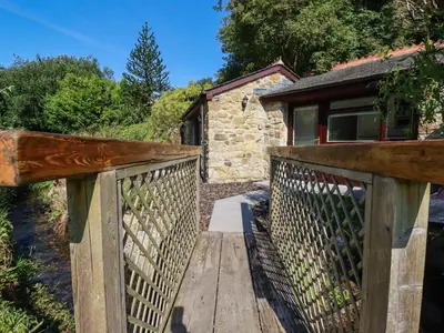 a wooden walkway leading to a cottage with a stone building at Peony Cottage in St Austell