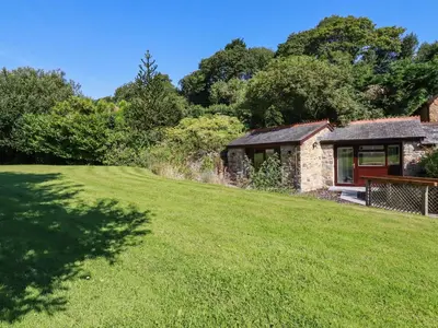 a stone cottage with a grassy yard in front of it at Peony Cottage in St Austell