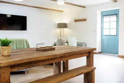 a living room with a wooden table and a tv at Budock Cottage in Mawnan