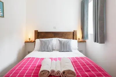 a bedroom with a pink and white bed with towels on it at Budock Cottage in Mawnan