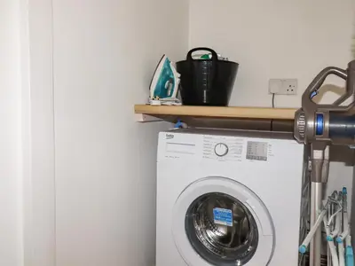 a laundry room with a washing machine and a wooden shelf at Rose Bud Cottage in St Austell