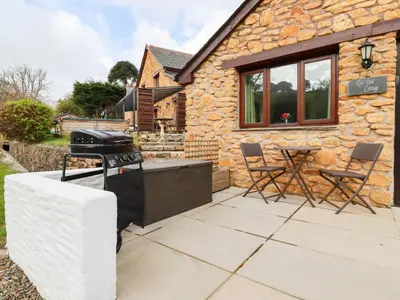 a barbecue on a patio outside of a stone cottage at Rose Bud Cottage in St Austell