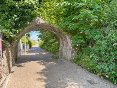 a stone archway over a brick road with trees at Summer Breeze in Newquay