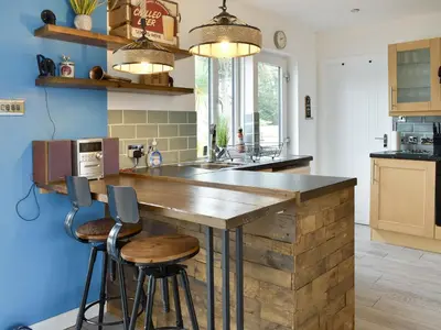 a kitchen with a wooden counter with stools around it at The Lily Pad in St Merryn
