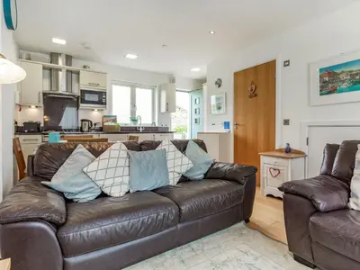 a living room with a brown leather couch and a kitchen at Constantine Bay Cottage in Padstow