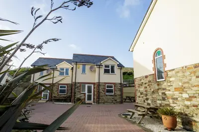 a house with a brick courtyard next to a church at Tregurrian Villas in Newquay