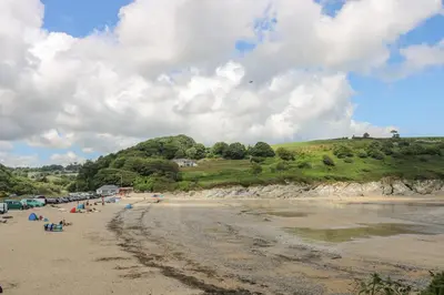 a beach with a group of people sitting on the sand at Charleston Cottage in Falmouth