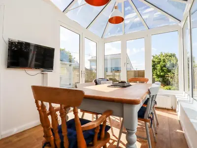 a conservatory with a table and chairs and a tv at Seawynds in Newquay