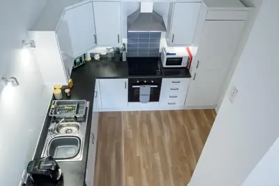 a small kitchen with white cabinets and a wooden floor at Mousehole in Mawnan