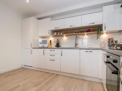 a white kitchen with white cabinets and a wooden floor at Azure in St Ives