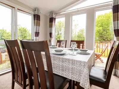 a dining room with a table and chairs and windows at 23 Bossiney Bay in Tintagel