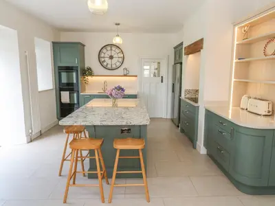 a kitchen with green cabinets and a counter with stools at Penmarth House in Helston