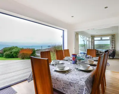 a dining room with a table with chairs and a large window at Sea Mist in Polzeath