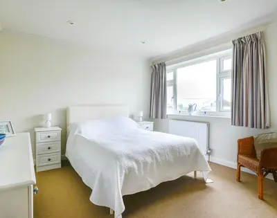 a white bedroom with a bed and a window at Sea Mist in Polzeath