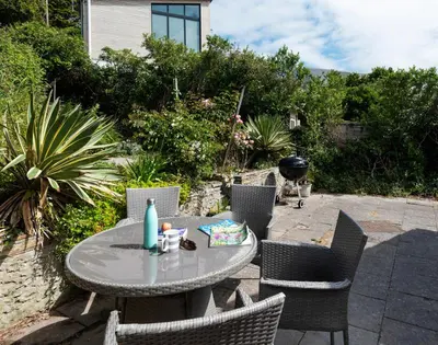a patio with a table and chairs and a grill at Brookside in Polzeath