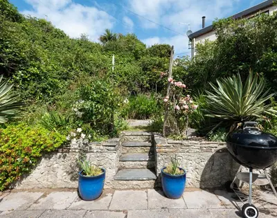 a garden with two blue potted plants and a grill at Brookside in Polzeath