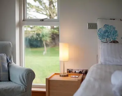 a bedroom with a chair and a lamp and a window at Ossco in Polzeath