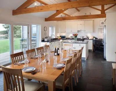 a large wooden table with chairs and a kitchen at Ossco in Polzeath