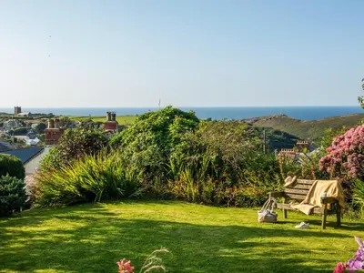 a garden with a bench and the ocean in the background at Trevivian House in Boscastle