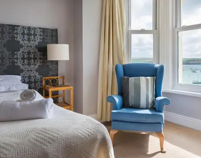 a bedroom with a blue chair and a bed and a window at 4 The Terrace in Padstow