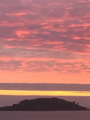 a sunset over an island in the ocean at Ocean View Apartments in Looe