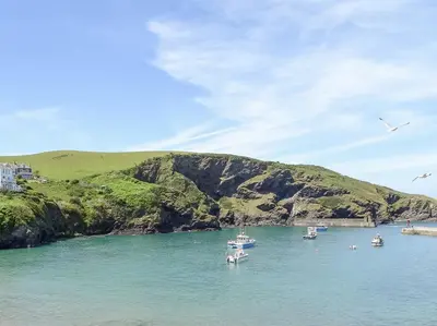 a group of boats in the water next to a hill at Kelmscot in Port Isaac