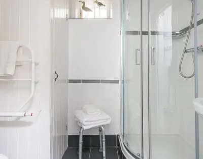 a white bathroom with a shower and a stool at Cloam Cottage in Port Isaac