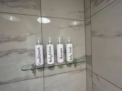 three white bottles on a glass shelf in a bathroom at Camellia Cottage in Camborne