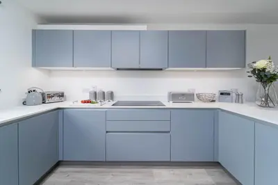 a white kitchen with blue cabinets and a sink at Tides in Carbis Bay