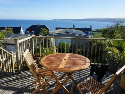 a wooden table and two chairs on a deck with the ocean at The Porthole in Port Isaac