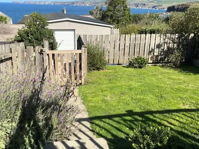 a backyard with a wooden fence and a yard with grass at The Porthole in Port Isaac
