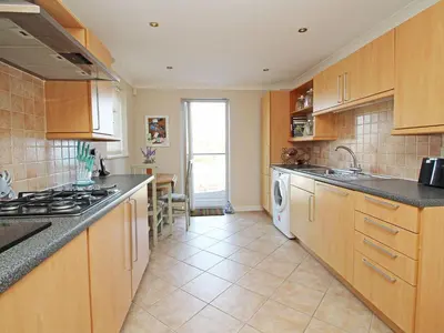 a kitchen with wooden cabinets and a washer and dryer at Wheal Kendall in St Austell
