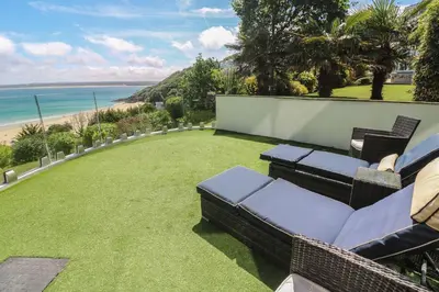 a patio with grass and chairs and the beach at Peninsula Apartment 2 in St Ives