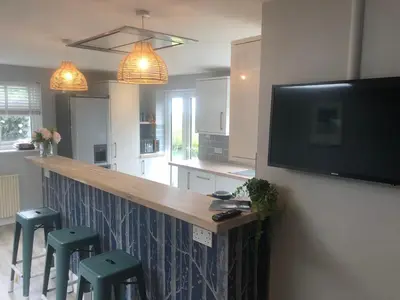 a kitchen with a bar with stools and a flat screen tv at Detached, peaceful, spacious with easy access and very large garden in Wadebridge