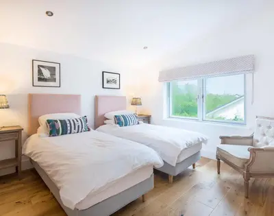 two beds in a room with a window and a chair at Artemis in Saint Minver
