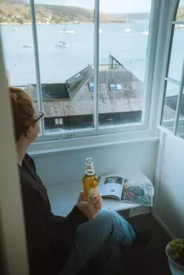 a woman sitting on a window sill with a bottle of honey at The Old Pirates Lookout in Falmouth
