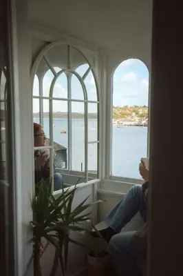 a woman sitting in a window looking out at the water at The Old Pirates Lookout in Falmouth