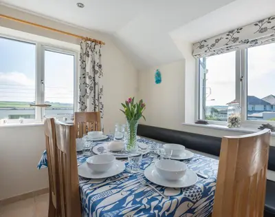 a dining room with a table with chairs and windows at Polmorla in Polzeath