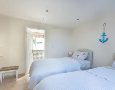 a white bedroom with two beds and a window at Polmorla in Polzeath