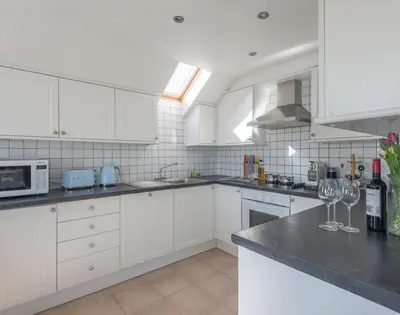 a kitchen with white cabinets and wine glasses on a counter at Polmorla in Polzeath