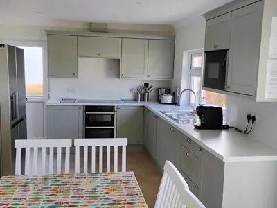 a kitchen with white cabinets and a table with a dining room at Chy-An-Var in Polzeath