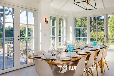 a dining room with a long wooden table and white chairs at Greystones in Polzeath