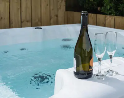 a bottle of wine and two glasses on a table next to a tub at Westray House in Polzeath