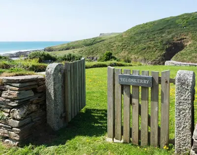 a wooden fence next to a stone wall and the ocean at Egloskerry in Wadebridge
